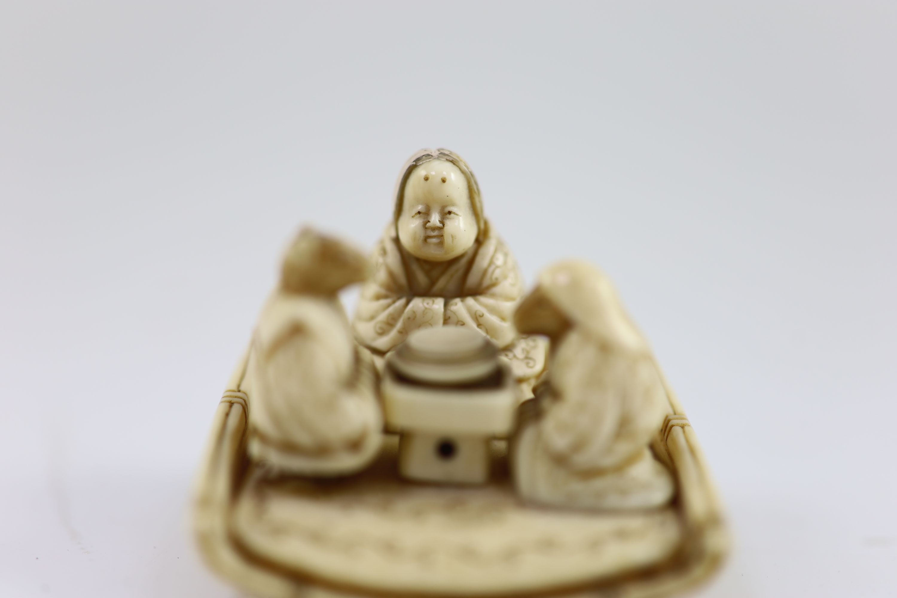 A Japanese ivory netsuke of figures seated around a table, Meiji period, 4.5 cm